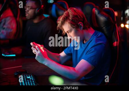 Ein schweres emotionales Spiel auf einem Smartphone von einem kaukasischen Kerl an einem Computer und in einem Gaming-Stuhl durchgeführt. Stockfoto
