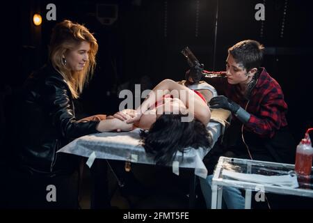 Das Mädchen kam zum Tattoo-Salon, um sich ein Tattoo zu holen und bat ihre Freundin, mit ihr zu sitzen, damit es nicht beängstigend und schmerzhaft wäre. Stockfoto