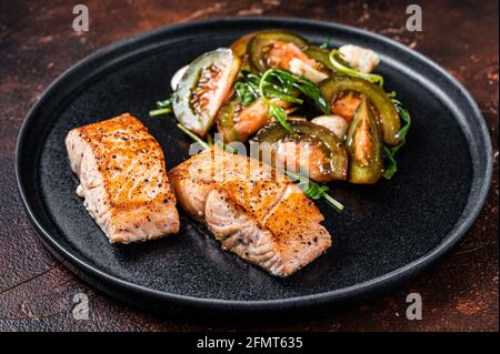 Gegrillte Lachsfilet Steaks mit Rucola und Tomatensalat auf einem Teller. Dunkler Hintergrund. Draufsicht Stockfoto