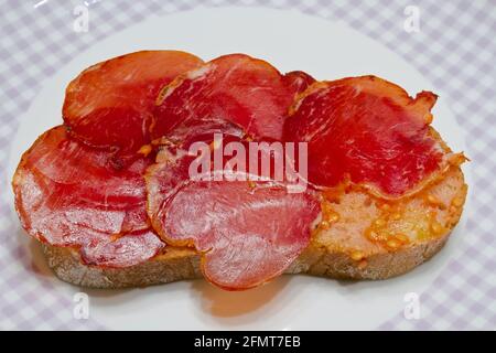 Spanische katalanische Tomaten verteilen sich auf eine Scheibe Brot mit Öl und das Salz auf den Scheiben iberischer Schweinelende. Stockfoto