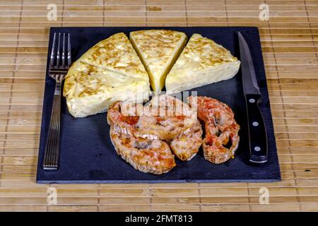 Ein Dreieck aus spanischem Kartoffelomelett, das auf Schieferplatte zubereitet wird Und mit Brot mit Tomaten bedeckt Stockfoto