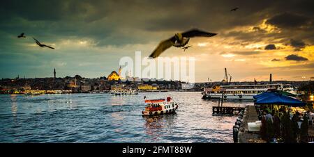 Atemberaubender goldener Sonnenuntergang über dem Bosporus, Istanbul mit Fährenbooten, die die Meerenge überqueren und Möwen, die im bewölkten Himmel fliegen. Stockfoto