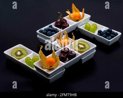 „Five a Day“ ist eine Auswahl von 5 frischen, gesunden Früchten, die auf einzigartige Weise in 5 weißen Porzellanschalen präsentiert werden, die eine Fünffache bilden. Schwarzer Hintergrund Stockfoto