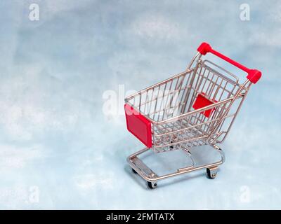 Ein leerer Mini-Supermarkt-Wagen auf blauem Hintergrund. Stockfoto