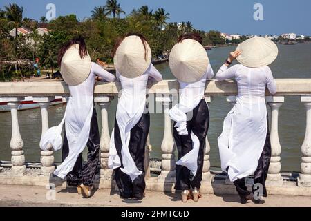 Rückansicht von vier vietnamesischen Frauen mit konischen Hüten und Ao dai traditionellen Kleidern auf der Brücke in der Altstadt von Hoi an, Vietnam Stockfoto