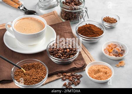 Kaffeetasse und verschiedene Kaffee- und Zuckersorten auf grauem Hintergrund. Seitenansicht, Nahaufnahme. Stockfoto