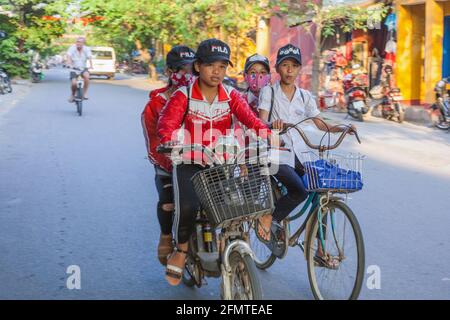 Vietnamesische Schulkinder reiten Seite an Seite auf ihren Fahrrädern durch die Altstadt von Hoi an, Vietnam Stockfoto