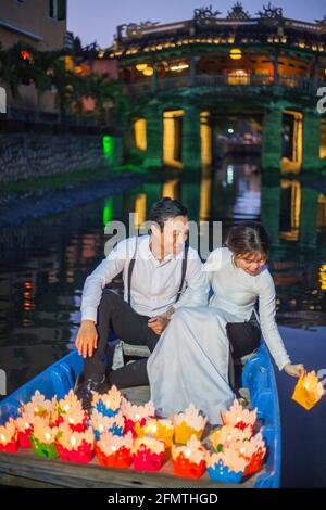 Das vietnamesische Paar saß im Boot vor der japanischen Brücke und ließ farbenfrohe, schwebende Laternen in den Fluss Hoi an, Vietnam, frei Stockfoto