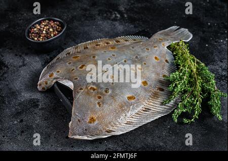 Roher Flunder Plattfisch auf Marmorplatte mit Thymian. Schwarzer Hintergrund. Draufsicht Stockfoto