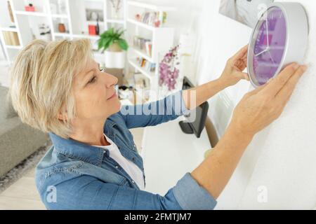 Ältere Frau, die eine Wanduhr aufstellte Stockfoto