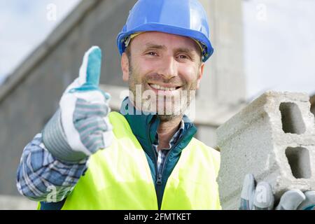 Ein Mann, der Daumen hoch zeigt, baut eine Ziegelwand Stockfoto