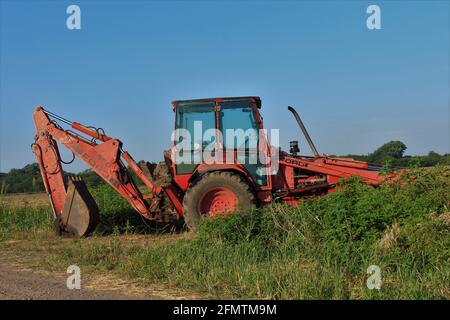 Ford-Traktor mit Frontlader und Bagger, die an einem Feld auf dem Bauernhof stehen, bereit für die Arbeit, die im Land in Kansas ist. Stockfoto