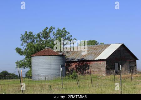 Kansas Country Barn mit einem Kornspeicher mit grünem Gras und blauem Himmel draußen im Land. Stockfoto