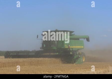 John Deere kombiniert auf einem landwirtschaftlichen Feld in Kansas Schneidweizen mit Weizenstaub in der Luft. Stockfoto