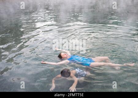 Eine Mutter und ein Sohn schwimmen im Trinity Hot Springs Pool Mit steigendem Dampf Stockfoto