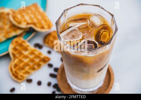 Erfrischender, eisgekühlter Latte-Kaffee in einem Glas mit Herzwaffeln Und Kaffeebohnen Stockfoto