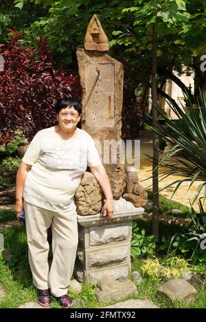 Eine ältere Frau steht neben einem Zeitstein Ein Park Stockfoto