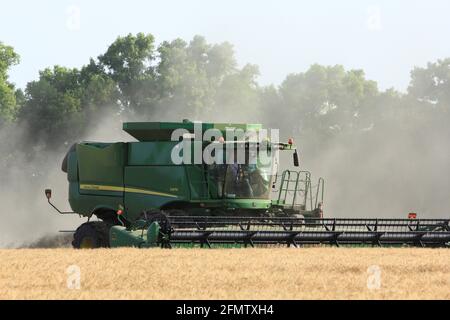 John Deere kombiniert auf einem landwirtschaftlichen Feld in Kansas Schneidweizen mit Weizenstaub in der Luft. Stockfoto