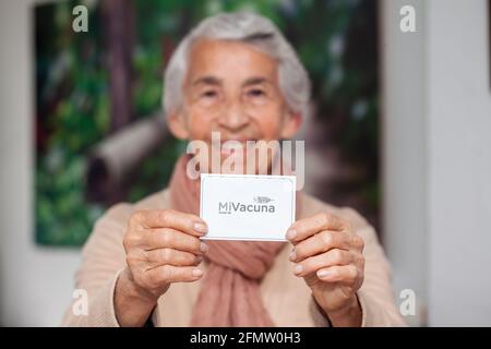 Ältere Frau in ihrem Haus mit ihrem Impfpass, nachdem sie den Covid-19-Impfstoff bei einer Impfung in Kolumbien erhalten hatte. Authentische Impfung ce Stockfoto