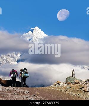 Blick auf den Berg Thamserku inmitten von Wolken, Mond und zwei Touristen, Khumbu-Tal, Solukhumbu, Himalaya-Berge in Nepal Stockfoto