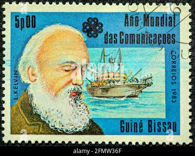 GUINEA - BISSAU - UM 1983: Eine in Guinea-Bissau gedruckte Briefmarke, die dem Weltkommunikationsjahr gewidmet ist, zeigt einen schottisch-irischen mathematischen Physiker A Stockfoto