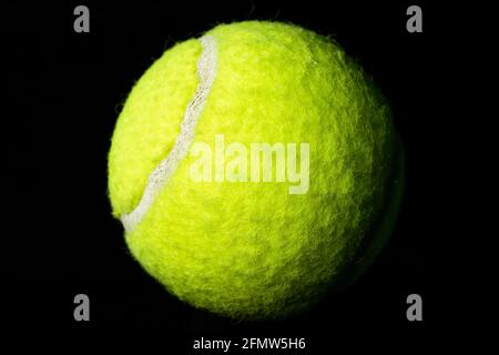 Isolierter, gelber Tennisball mit Optik vor schwarzem Hintergrund Stockfoto