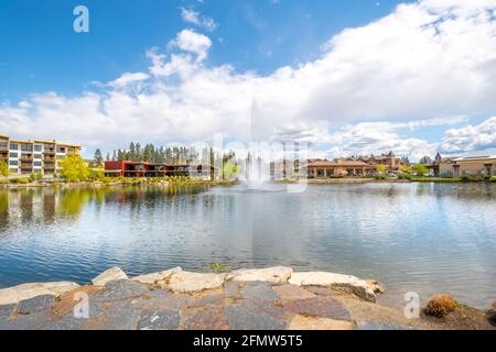 Riverstone öffentlicher Park in Coeur d'Alene, Idaho, USA, mit Restaurants, Neubau und dem Wasserbrunnen, der in den kleinen See sprüht. Stockfoto