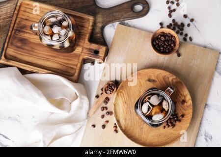 Mason Gläser mit leckeren kalten Brühe und Kaffeebohnen auf Heller Holzhintergrund Stockfoto