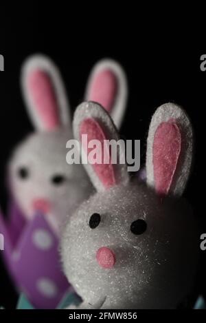 Ein vertikales Standleben-Bild auf einem schwarzen Hintergrund von zwei weißen fuzzy-Spielzeug-Kaninchen, einem Osterhasen-Spielzeug Stockfoto