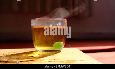 Glaskanne auf Holzplatte und rotem Teppich mit schwarzem Schattenhintergrund vorhanden. Isolierte Linden-Teetasse aus Glas und es ist grün mtholated Stockfoto