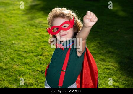 Tapferer Junge in einem Superhelden-Kostüm, mit rotem Cape und Maske, streckt seine Hand aus. Niedliches Kind spielt Superheld. Das Konzept von Macht und Gerechtigkeit. Stockfoto