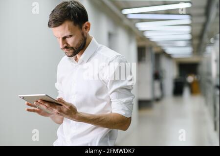 Ein Mann in einem weißen Hemd hält ein Tablet und lächelt im Büro. Geschäftsmann auf dem Hintergrund des Büros Stockfoto