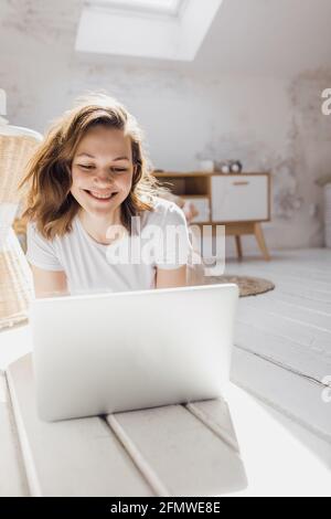 Das attraktive afroamerikanische Mädchen nutzt einen Laptop und lächelt beim Sitzen Der Boden Stockfoto