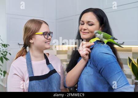 Freundliche fröhliche Familie, Porträt von Mutter und Tochter im Teenageralter, mit grünem Papagei Stockfoto