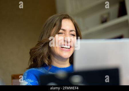 Frau, die vor sich lacht, als sie Medien über sie liest Laptop-Computer in einer Nahaufnahme aus dem niedrigen Winkel mit Fokussiere dich auf ihr Gesicht Stockfoto