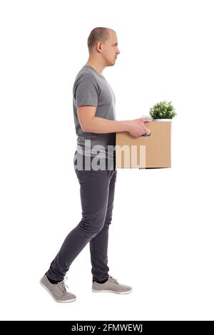 Seitenansicht eines jungen, gutaussehenden, wandenden Mannes, der einen Kasten mit hält Habseligkeiten auf weißem Hintergrund isoliert Stockfoto