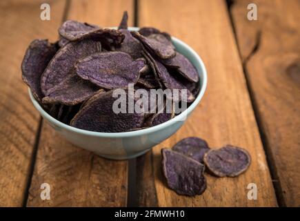 Kartoffelchips aus violetten Kartoffeln in einer türkisfarbenen Schüssel Auf rustikalem Holztisch Stockfoto