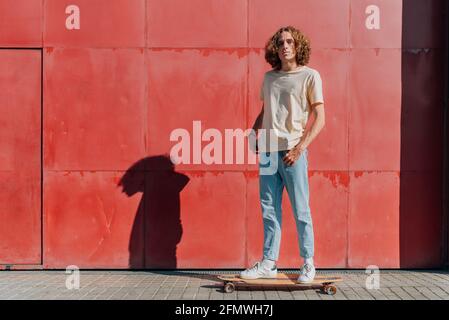 Horizontales Porträt eines kaukasischen Mannes, der auf seinem Skateboard steht. Er blickt selbstbewusst auf die Kamera. Stockfoto