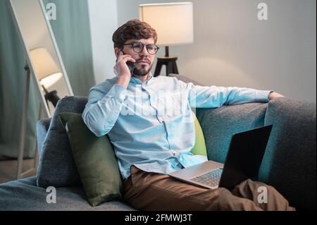 Ein netter Manager arbeitet aus der Ferne, legt den Laptop auf sich und ruft seinen Kunden an. Stockfoto
