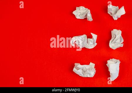 Zerknitterte Reste weißen Papiers auf rotem Hintergrund. Sechs zerknitterte Papierstücke liegen zufällig. Draufsicht, flach liegend. Stockfoto