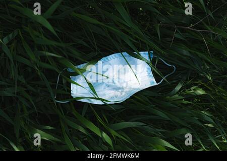 Gebrauchte medizinische Gesichtsmaske im grünen Gras. Biohazard, Mikroplastik, post covid Umweltbelange, Naturverschmutzung Stockfoto