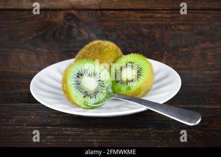 Zwei Kiwi-Früchte mit Löffel auf weißem Teller, ein Kiwi in zwei Hälften geschnitten. Stockfoto