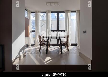 Esstisch und Stühle vor dem Panoramafenster In einem modernen, hellen Apartment mit minimalistischen, mit weißen Vorhängen eingerichtet Innenarchitektur Stockfoto