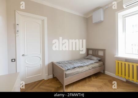 Minimalistisches Innendesign eines modernen, hellen Schlafzimmers mit Holz Einzelbett in der Ecke zwischen Tür und Fenster mit platziert Gelber Kühler Stockfoto