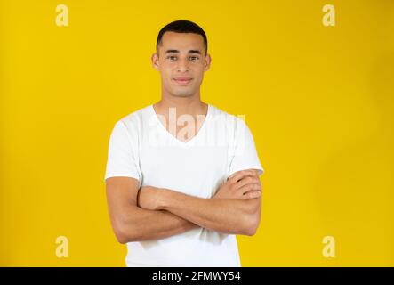 Attraktiver junger Mann im lässigen T-Shirt mit vereinzelten Armen auf gelbem Hintergrund. Stockfoto