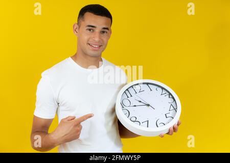 Junger Mann in weißem T-Shirt mit einer großen Uhr isoliert auf gelbem Hintergrund. Stockfoto