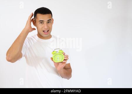 Überraschender junger Mann, der einen Wecker auf weißem Hintergrund hält. Stockfoto