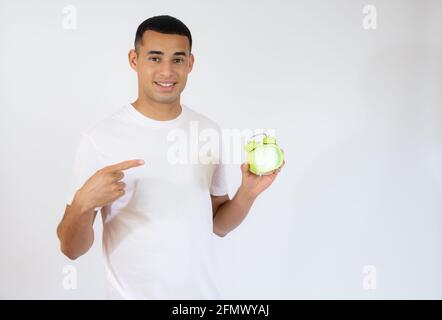 Lächelnder junger Mann, der einen Wecker auf weißem Hintergrund hält. Stockfoto