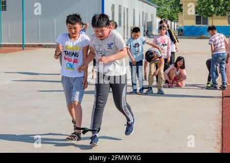 Grundschüler, die in einer ländlichen Schule in Shandong, China, ein dreibeiniges Rennen führen. Stockfoto