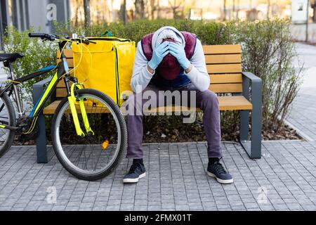 Junger Kurier in medizinischer Maske liefert Lebensmittel mit gelbem Thermalrucksack, fährt mit dem Fahrrad in der Stadt. Konzept für den Lieferservice von Lebensmitteln Stockfoto